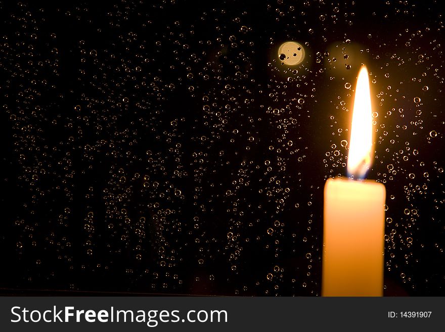 Rain drops reflect light of a burning candle in glass at night. Rain drops reflect light of a burning candle in glass at night