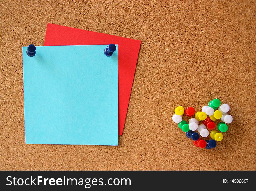 Red and blue post-it notes with many pushpins in a shape of a heart on corkboard