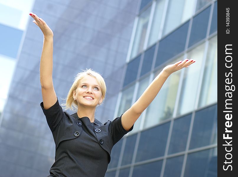 A young and attractive business woman is holding her hands up as a sign of success. Image taken outdoors, on a modern background.