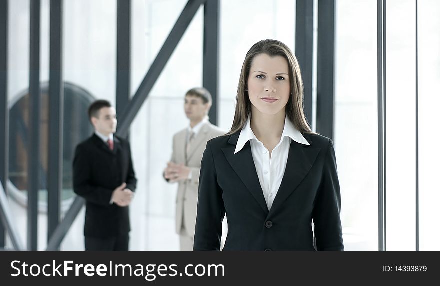 A young and attractive business woman is standing in front of her male colleagues. Image taken in a modern office. A young and attractive business woman is standing in front of her male colleagues. Image taken in a modern office.