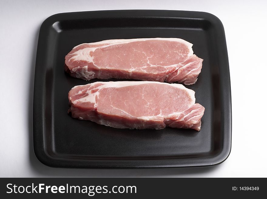 Two raw pork steaks on the black square plate over white background