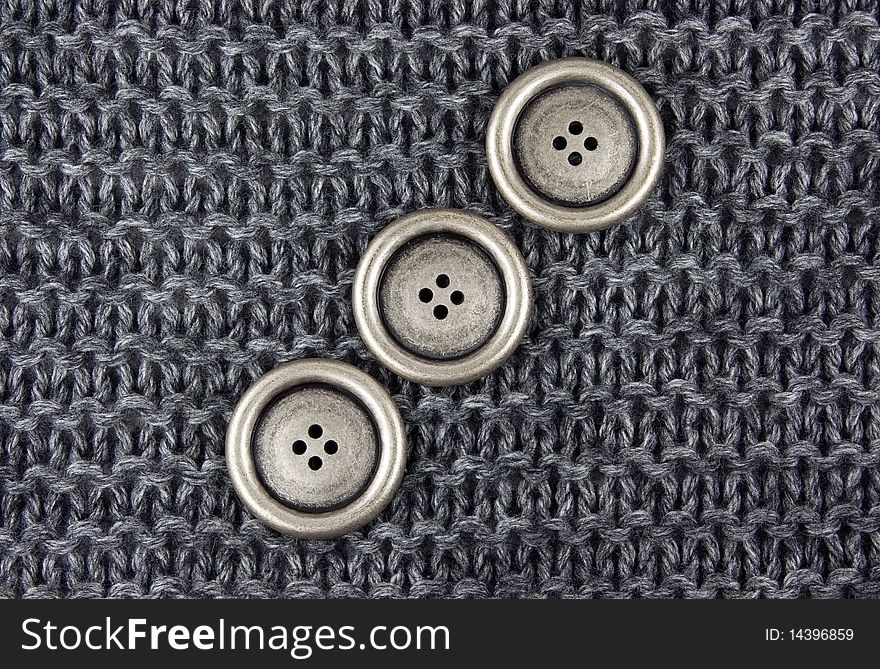 Three metal buttons on a gray knitted fabric background. Three metal buttons on a gray knitted fabric background