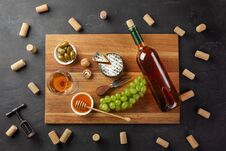 White Wine Bottle, Cheese Head, Bunch Of Grapes, Honey, Nuts And Wineglass On Cutting Board With Corks And Corkscrew On Black Stock Image White Wine Bottle, Cheese Head, Bunch Of Grapes, Honey, Nuts And Wineglass On Cutting Board With Corks And Corkscrew On Black Stock Image