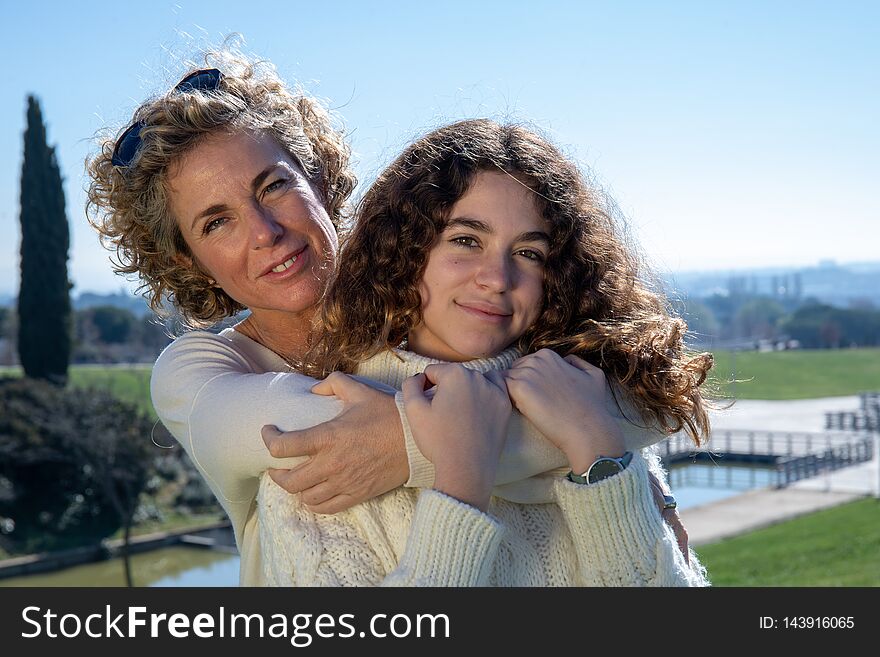 Mother and daughter embrace each other with the blue sky in the background and strongly illuminated by the sun. Mother and daughter embrace each other with the blue sky in the background and strongly illuminated by the sun