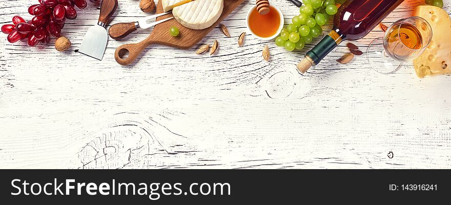 White wine bottle, grape, honey, cheese and wineglass on white wooden board. Panoramic top view with copy space for your text