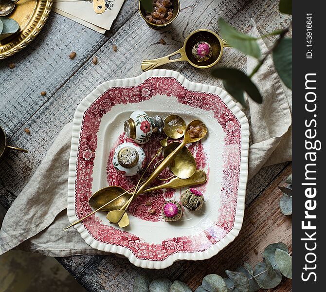 Overhead shot of vintage plate with pink ornament with brass spoons, strainers and chiness tea