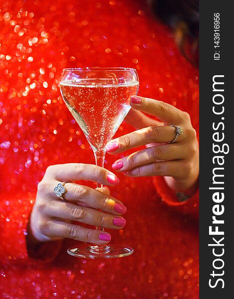 Glass hand girl. White wine in the glass and girl in a sparkling red dress close-up.