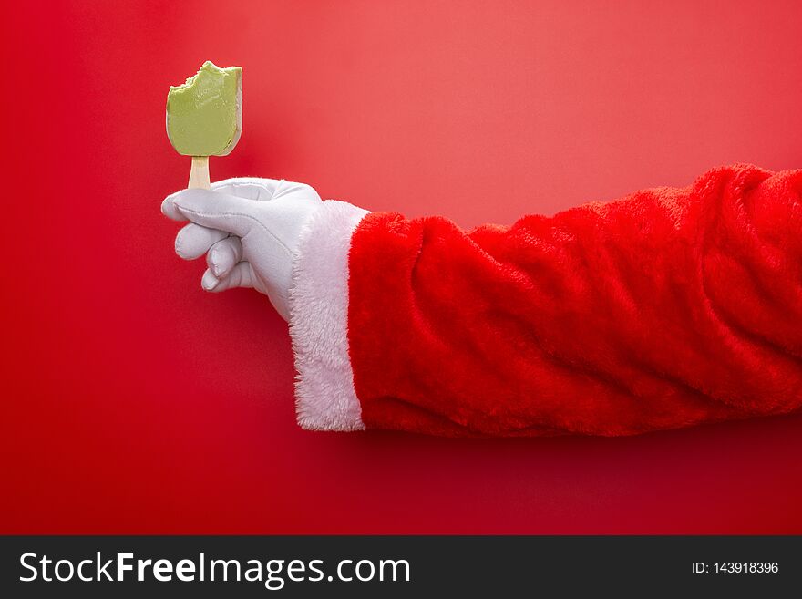 Santa claus holding green bean popsicle with some bites in front of a red background