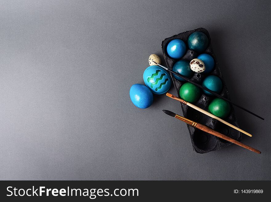 Easter holiday: colored painted eggs in a black box and a brush against a dark background. Top view.