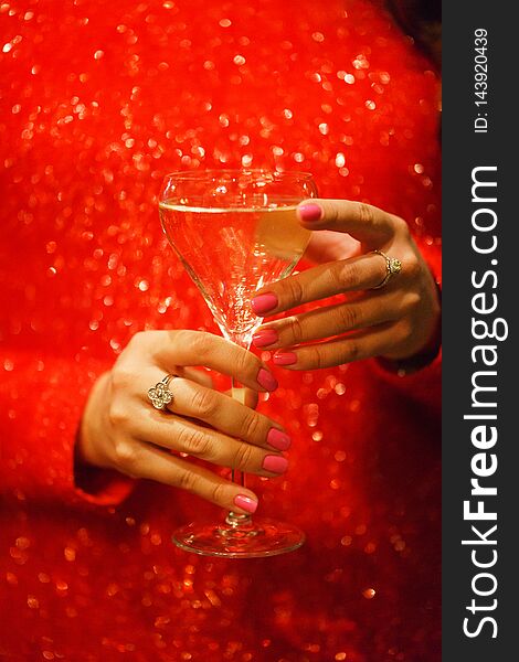 Glass hand girl. White wine in the glass and girl in a sparkling red dress close-up. Celebration and party in a nightclub. Chic red dress. Drinks for adults. Beautiful bokeh and soft focus.