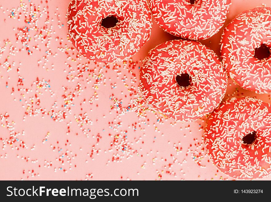 Five coral donuts lying in a corner. Donuts decorated with icing on pink background. Top view. Copy space for text