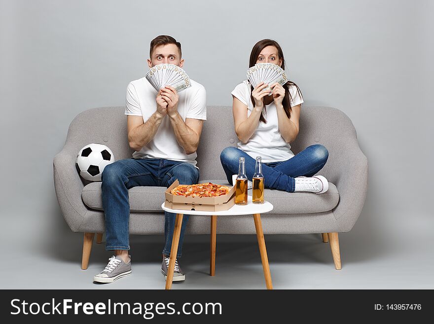 Shocked couple woman man football fans cheer up support favorite team, covering face with fan of money in dollar
