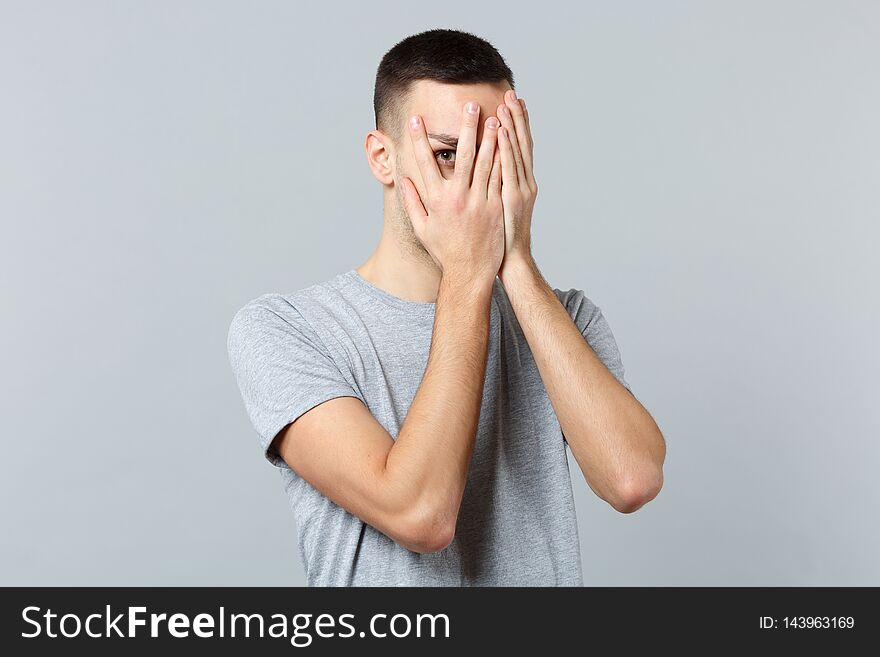 Portrait of young man in casual clothes hiding, covering face with hands isolated on grey wall background in studio. People sincere emotions, lifestyle concept. Mock up copy space. Advertising area