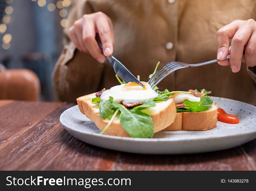 A Woman Eating Breakfast Sandwich With Eggs, Bacon And Sour Cream By Knife And Fork In A Plate