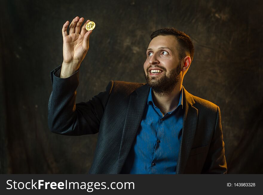 A young businessman holds a coin of bitcoite in his hand