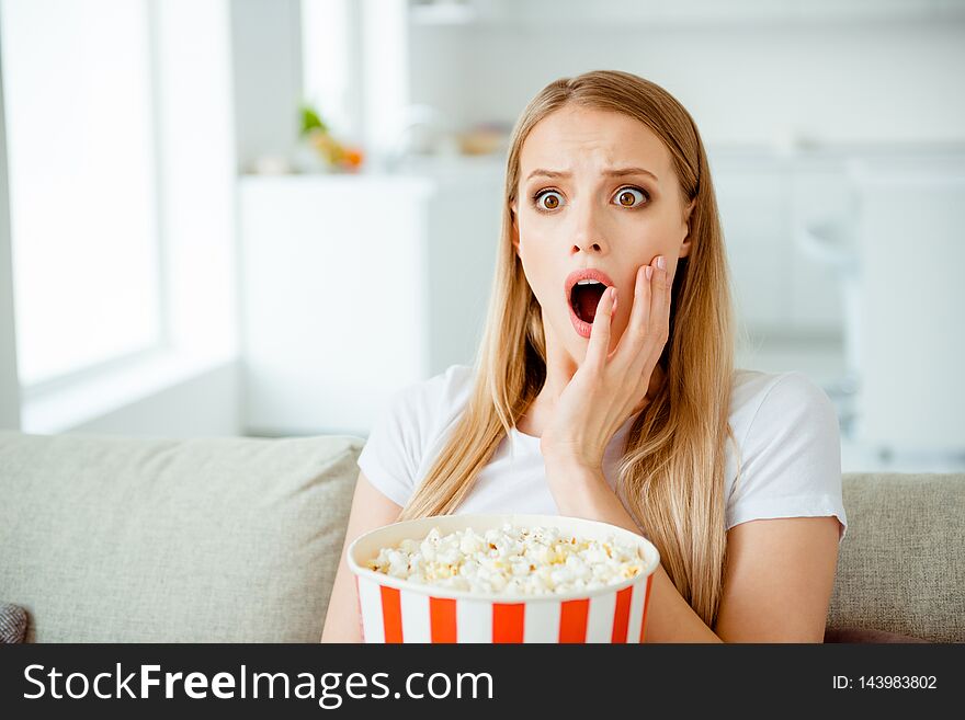 Close up photo of attractive nice student youth impressed astonished watch see incredible tv program entertainment scream shout touch cheeks sit in light apartment dressed trendy modern t-shirt.