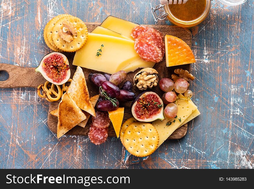 Cheese plate served with grapes, jam, figs, crackers and nuts on a grey background.