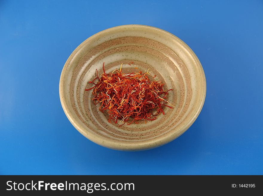 A small dish with the very expensive spice saffron inside on a blue background.