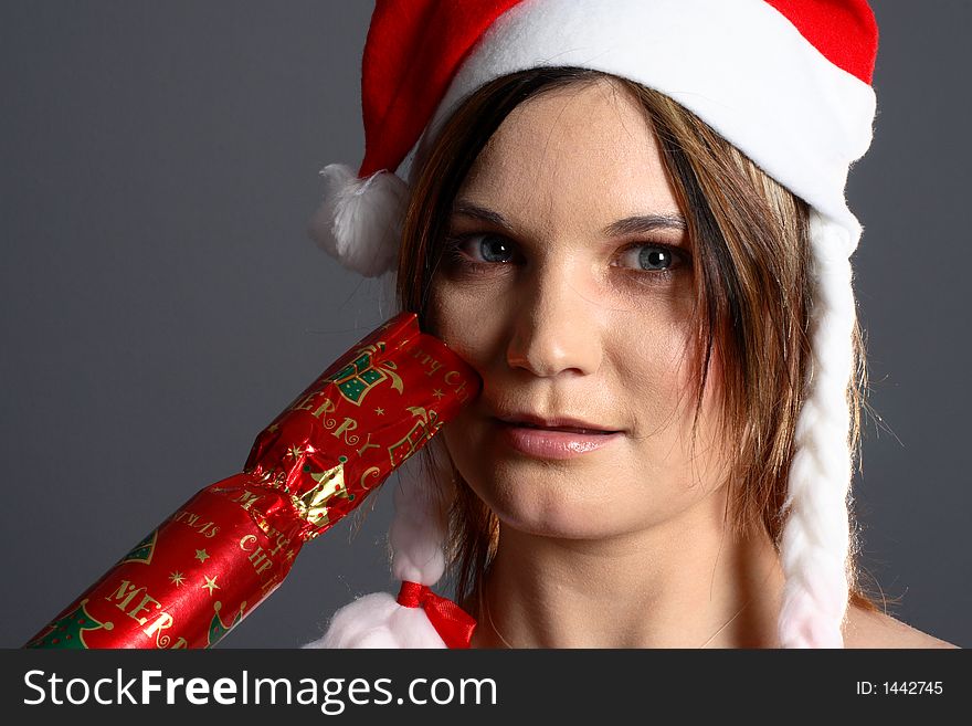 Young santa girl in front of grey background with christmas cracker. Young santa girl in front of grey background with christmas cracker