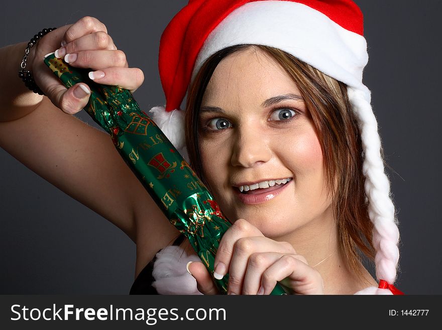Young santa girl in front of grey background with christmas cracker. Young santa girl in front of grey background with christmas cracker