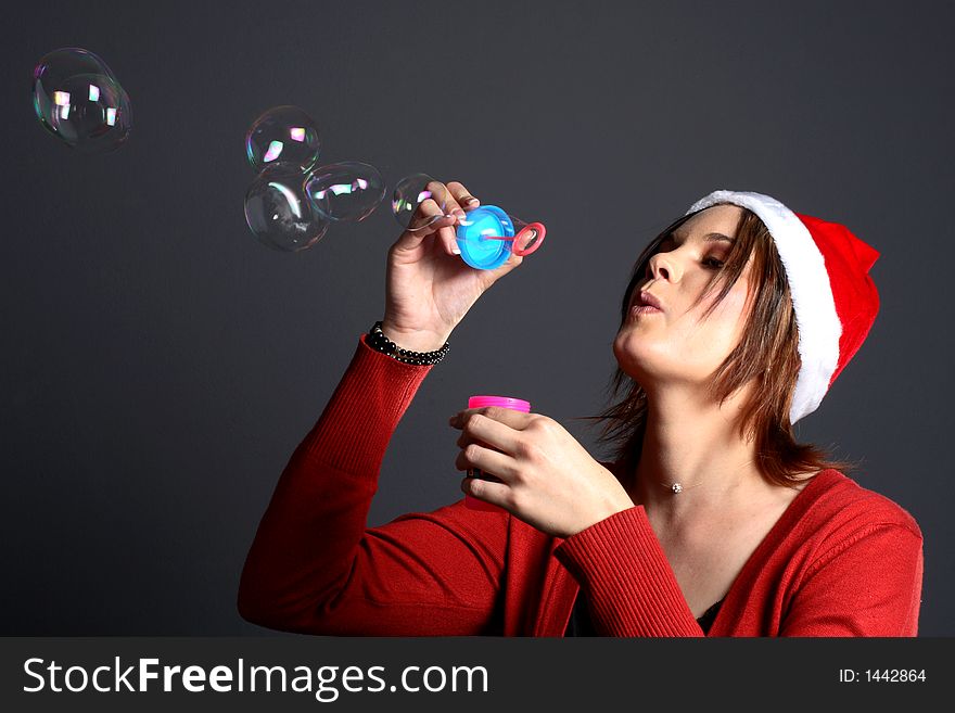 Young santa girl model in front of grey background blowing bubbles. Young santa girl model in front of grey background blowing bubbles