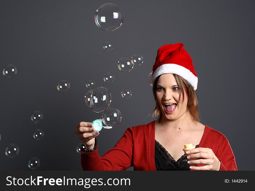 Young santa girl model in front of grey background blowing bubbles. Young santa girl model in front of grey background blowing bubbles