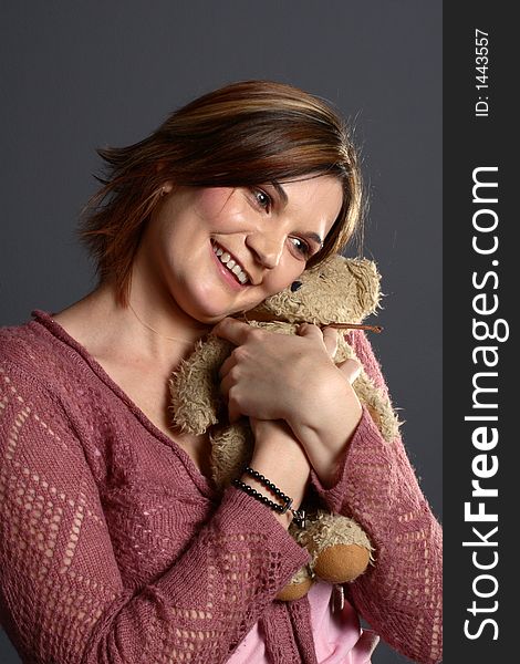 Brunette model hugging traditional teddy bear in front of grey background. Brunette model hugging traditional teddy bear in front of grey background