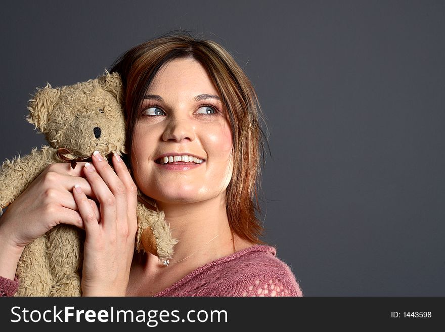 Brunette model hugging traditional teddy bear in front of grey background. Brunette model hugging traditional teddy bear in front of grey background