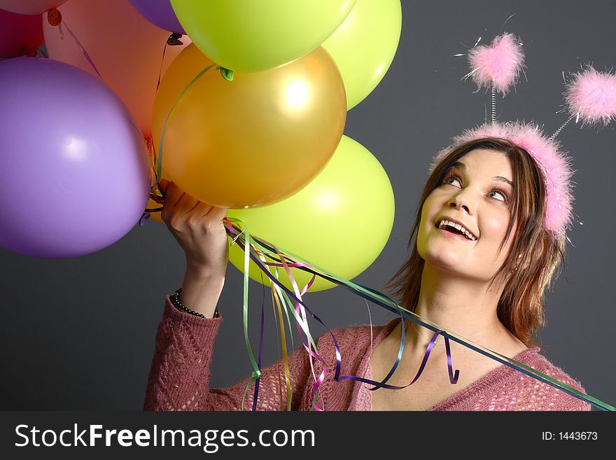 Brunette model with alien antenna and balloons in front of grey background. Brunette model with alien antenna and balloons in front of grey background