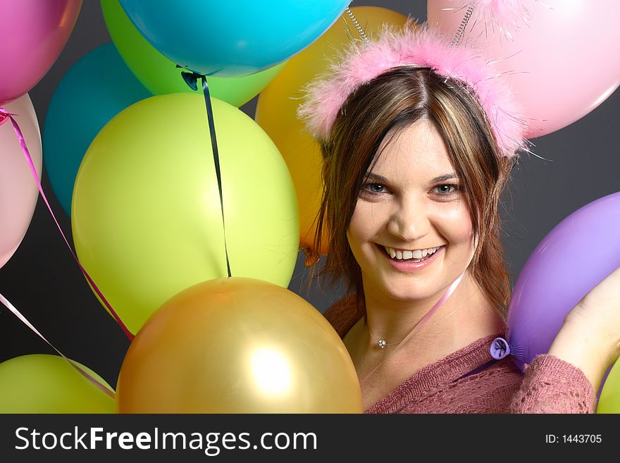 Brunette model with alien antenna and balloons in front of grey background. Brunette model with alien antenna and balloons in front of grey background