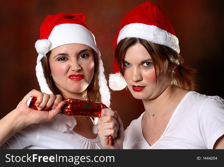 Two girls wearing santa caps fighting over a cracker. Two girls wearing santa caps fighting over a cracker