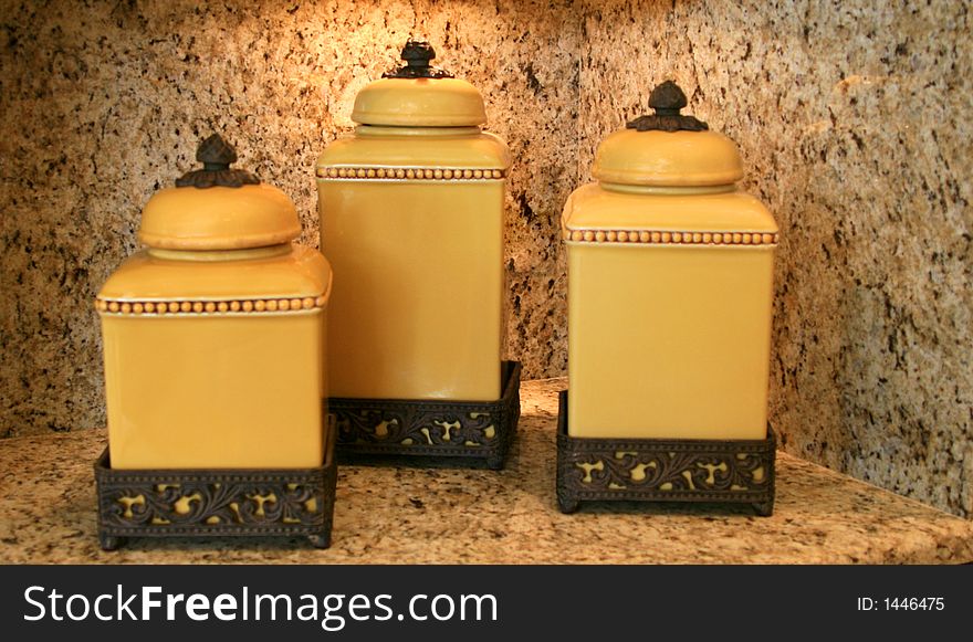 Set of gold-colored cannisters on carved wooden stands sitting on granite cabinet. Set of gold-colored cannisters on carved wooden stands sitting on granite cabinet