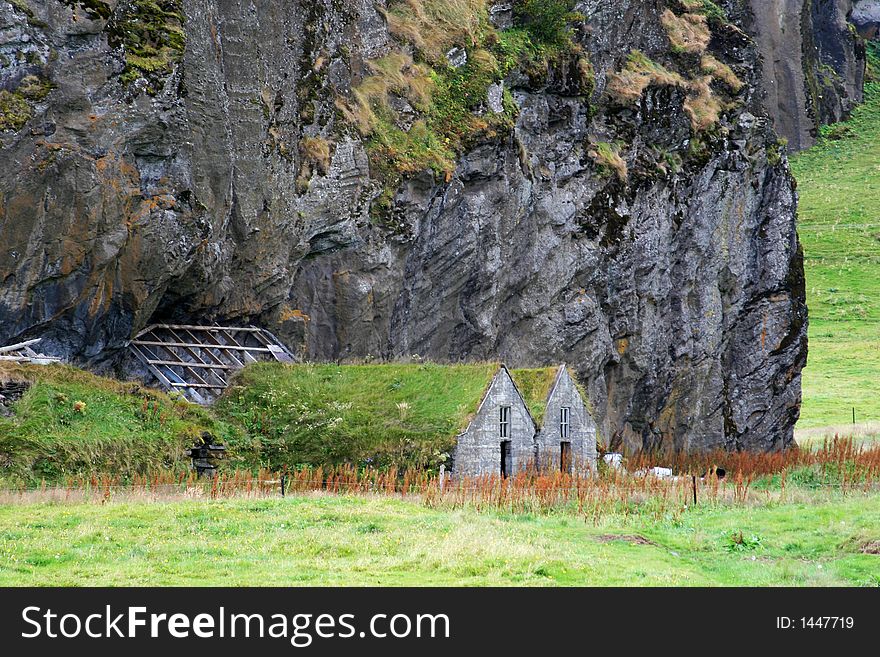 An old house with grass roof, under a massive cliff,/rock, in need of repairs. An old house with grass roof, under a massive cliff,/rock, in need of repairs