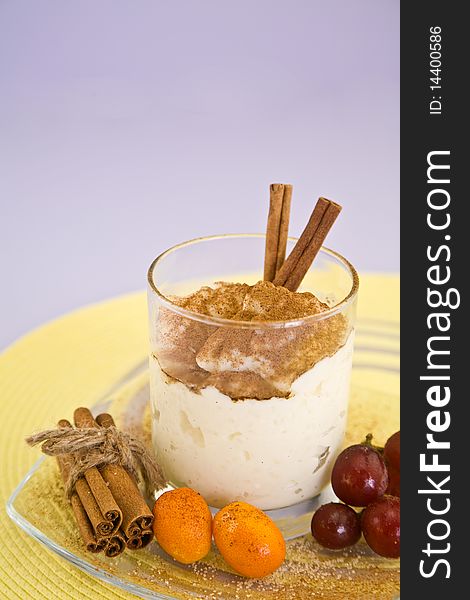 Rice pudding covered in cinnamon in glass. Rice dessert is surrounded by cinnamon sticks, cumquats and cherries. Rice pudding covered in cinnamon in glass. Rice dessert is surrounded by cinnamon sticks, cumquats and cherries.