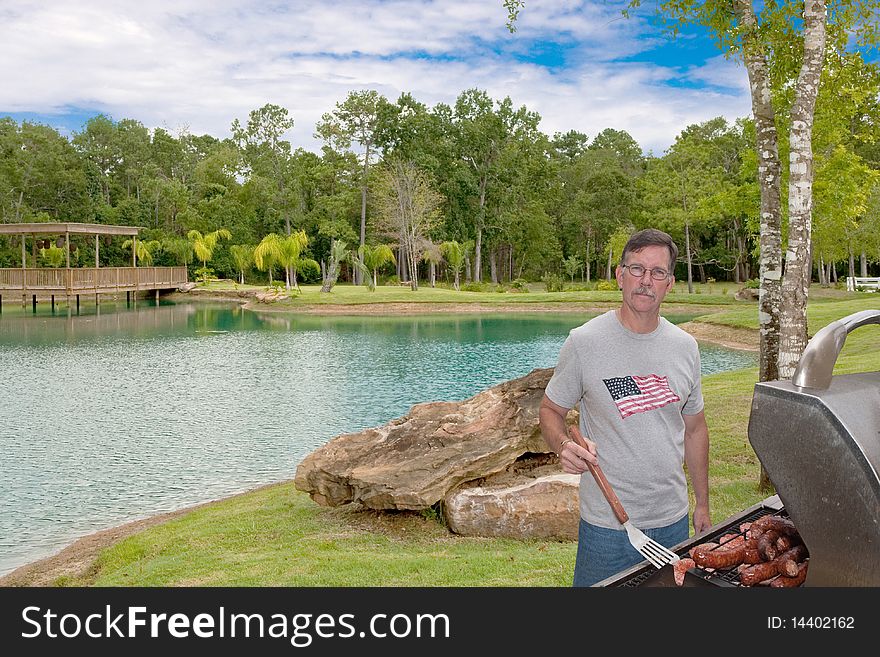Mature young man in Park barbecuing hamburgers and sausages on a gas grill. Could be July 4th or other holiday. Mature young man in Park barbecuing hamburgers and sausages on a gas grill. Could be July 4th or other holiday.