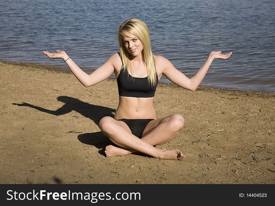 A woman sitting in the sand at the beach in a yoga position not sure if she is doing it right. A woman sitting in the sand at the beach in a yoga position not sure if she is doing it right.