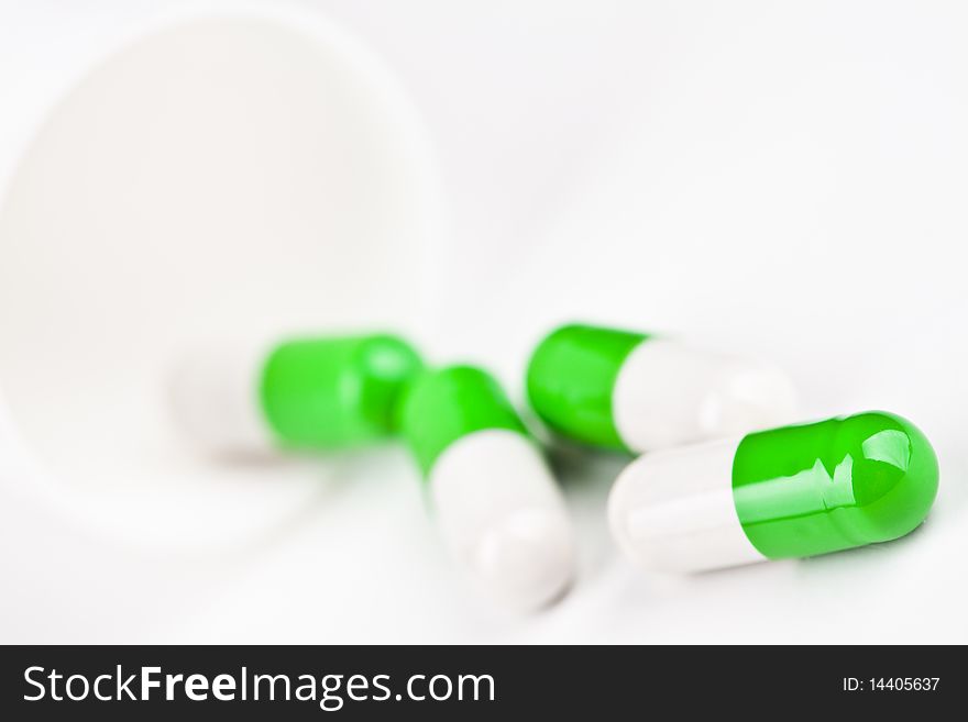 Capsules pouring out of a white glass on white background. Capsules pouring out of a white glass on white background