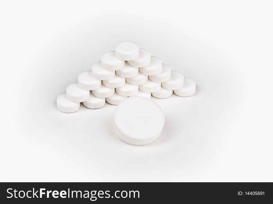 Large white tablet in front of a pyramid of white tablets over wite backround