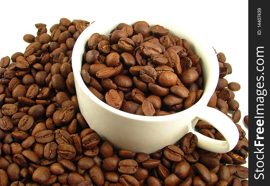 White cup filled and surrounded by whole coffee beans. White cup filled and surrounded by whole coffee beans
