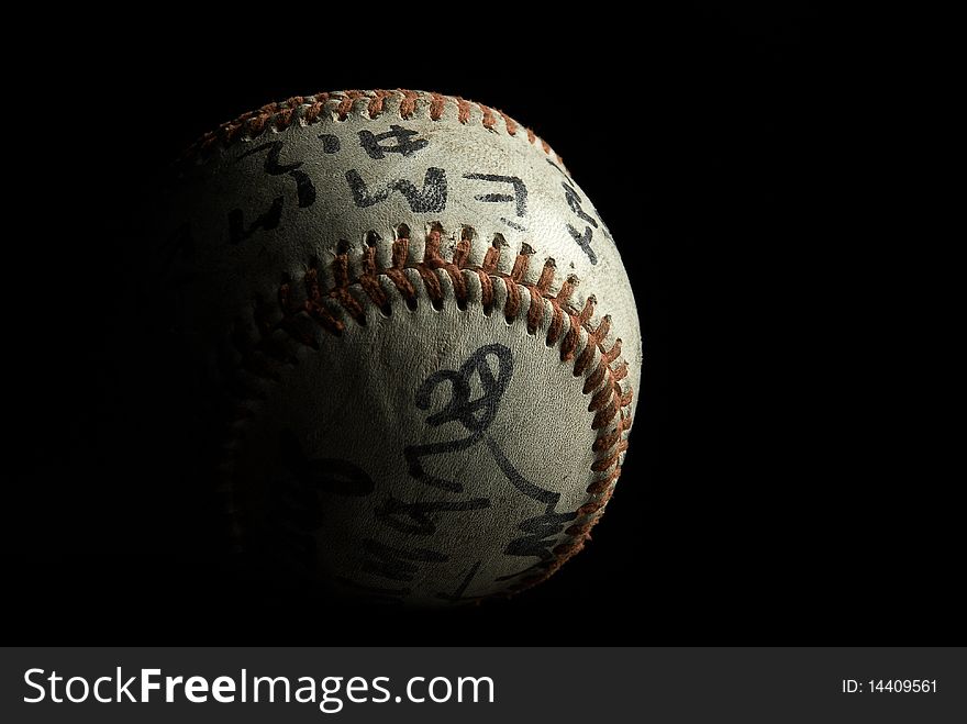 An old leather baseball with red stitching, side lit with black background and indistinguishable autographs. An old leather baseball with red stitching, side lit with black background and indistinguishable autographs.