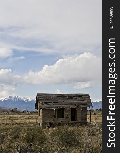 Abandoned one room plains house fallen into disrepair in Idaho with the snowcapped Targhee National Forest in the horizon