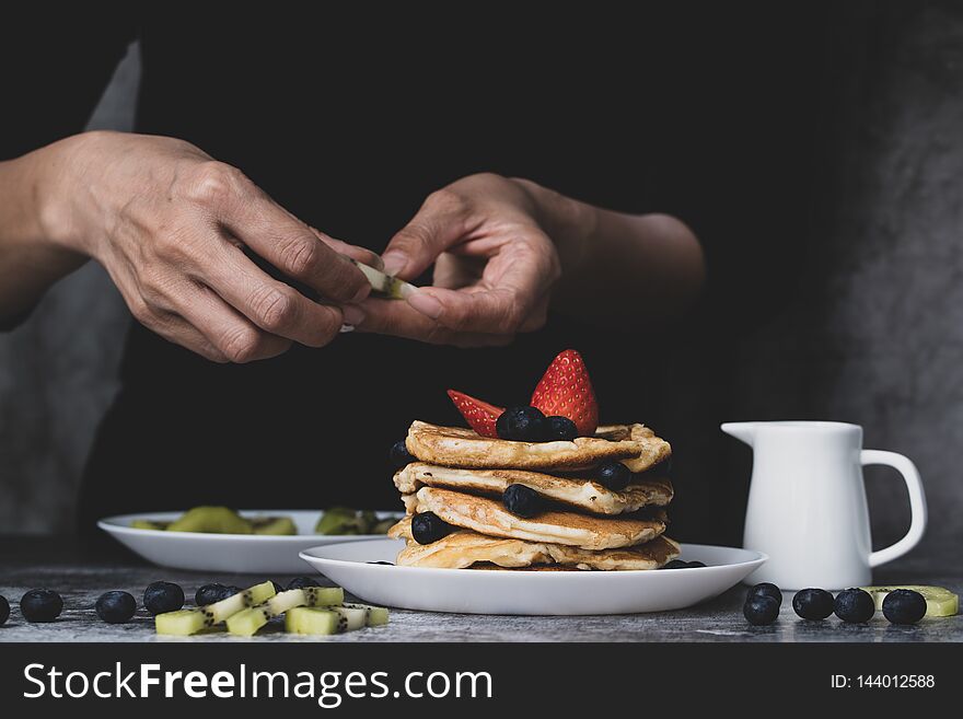 Woman housewife preparing pancakes to be food for family, putting topping fruit, strawberries, kiwi and blueberries on top. Woman housewife preparing pancakes to be food for family, putting topping fruit, strawberries, kiwi and blueberries on top