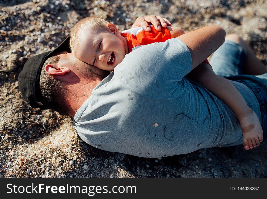 Funny portrait of a father and son, while they are playing on the beach, lying on the sand, embracing and smiling