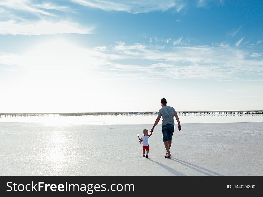 Portrait of a little boy with his father on the beach. They are walking to the sea back to the camera