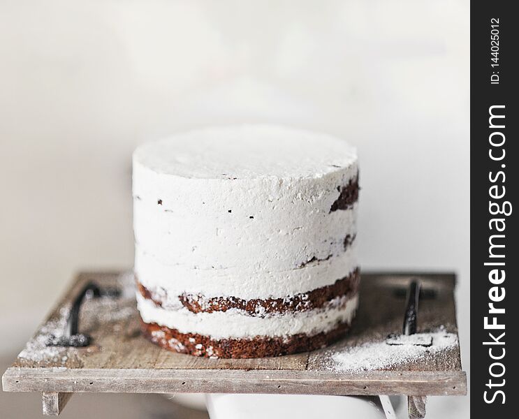 chocolate cake smeared with white cream. stands on a wooden stand