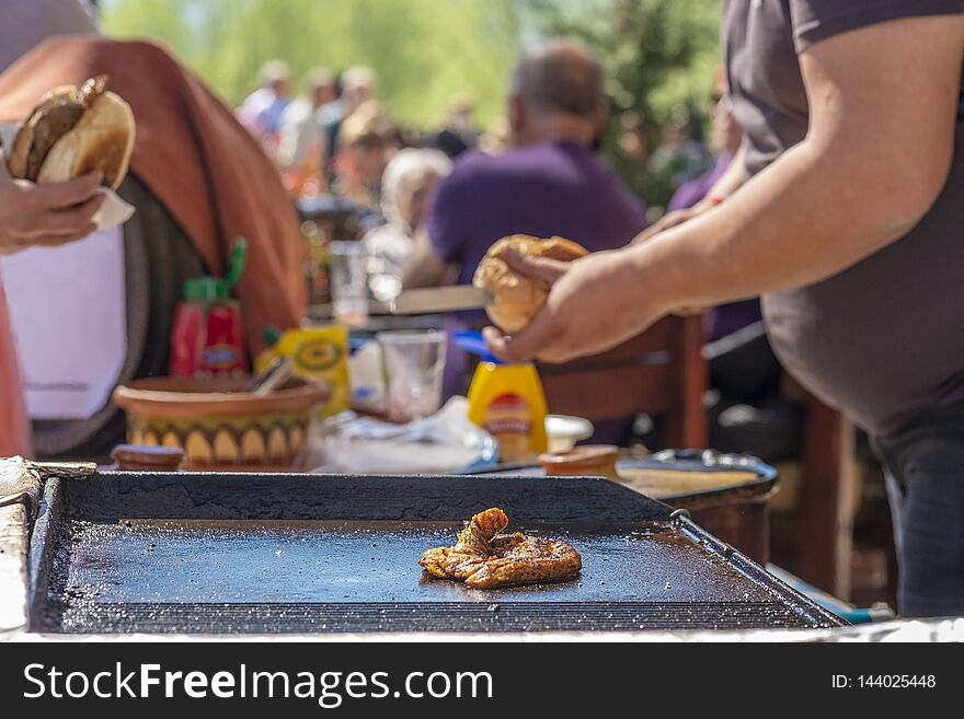 A fat young guy makes hamburgers with fried beef succulent appetizing cutlets and sells them to the guests of the festival. A fat young guy makes hamburgers with fried beef succulent appetizing cutlets and sells them to the guests of the festival