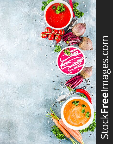 Set of various vegetable cream soups, Carrot, beet root, spicy tomato pureed soups with fresh organic veggies, blue concrete background, copy space