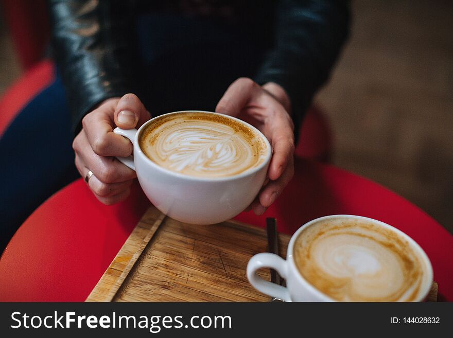Closeup image of a hand holding a white cups of hot latte coffee of cappuccino coffee on red table in cafe