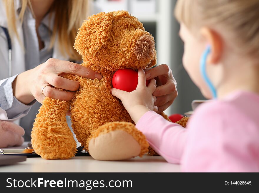 Little girl hold in arms toy red hear playing with teddy bear while visiting doctor