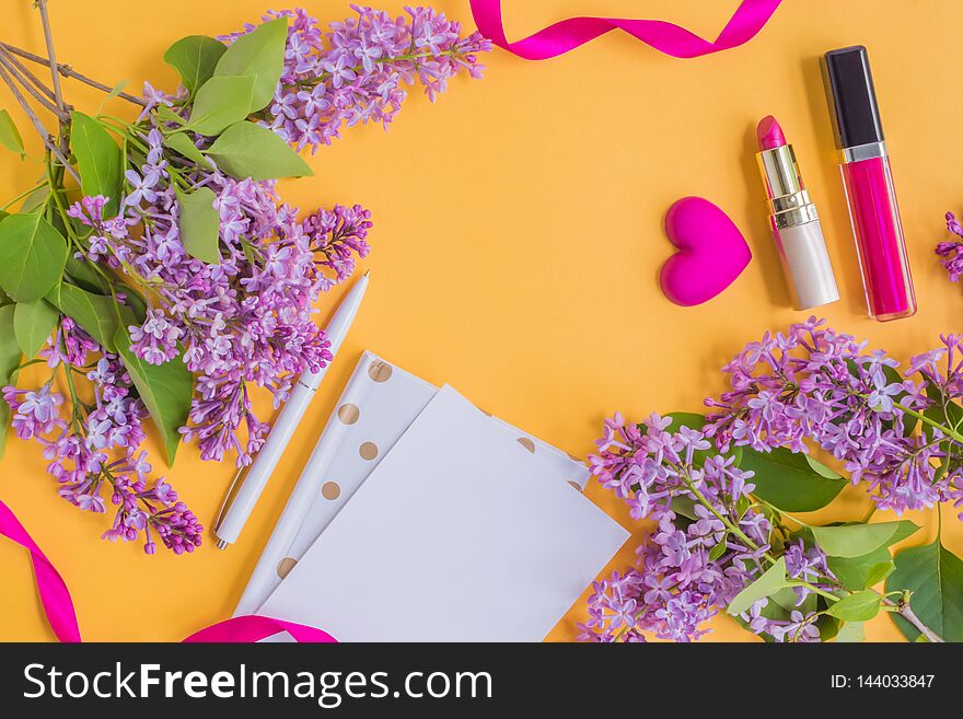 Flat lay desk with lilac branches, notebook and cosmetic on yellow background